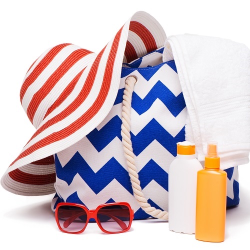 Photo of a bech bag, a wide-brimmed hat, sunglasses, sunscreen, and a towel