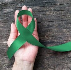 Green cancer ribbon in the palm of a hand