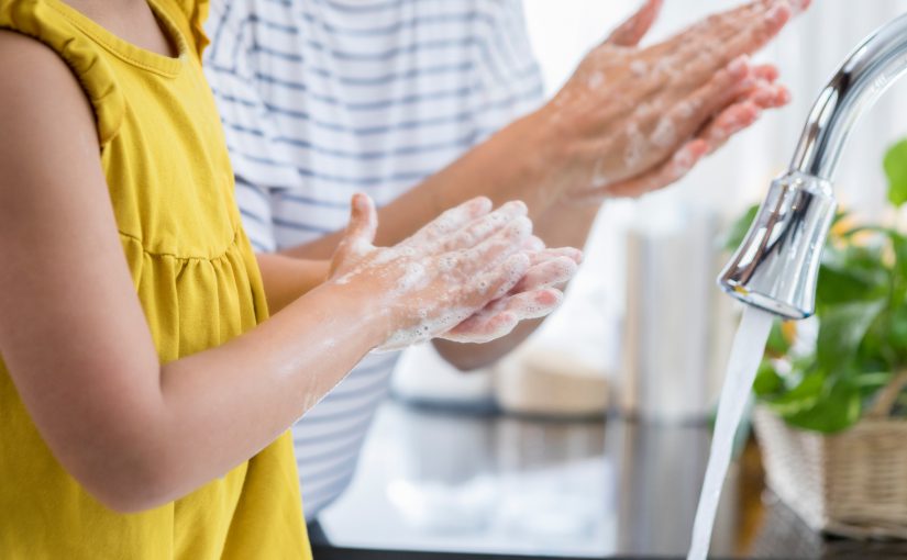 Unrecognizable mom helps her young daughter wash her hands. They are rubbing their hands together creating foam with the soap.