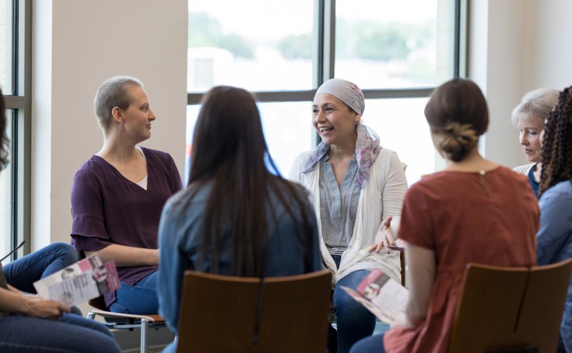 Woman wearing a headscarf gestures while discussing chemotherapy treatment with women in a breast cancer support group.