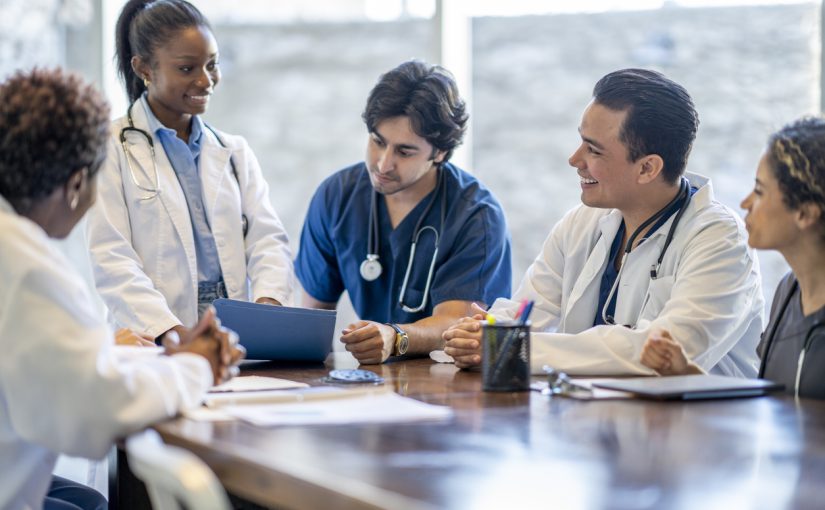 A small group of medical professionals sit at a table together discussing patient care.