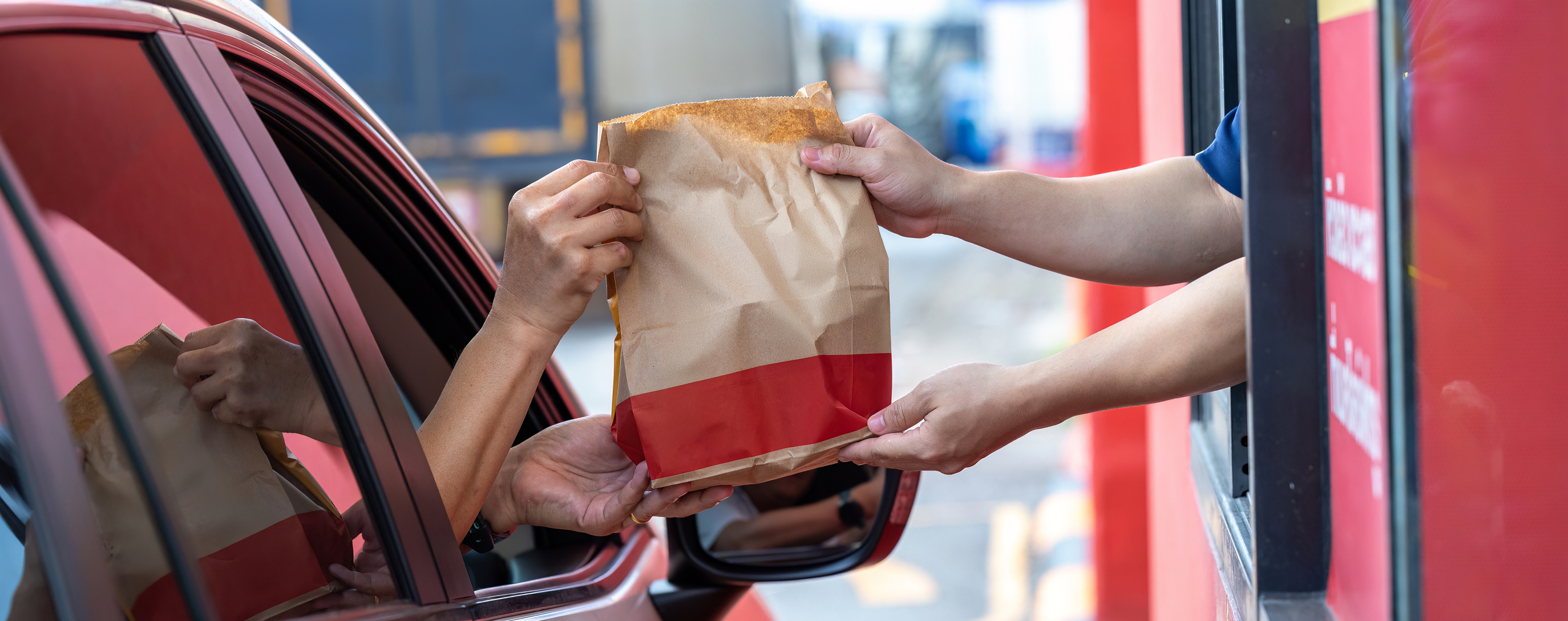 A person in car receiving bag in drive thru fast food restaurant.