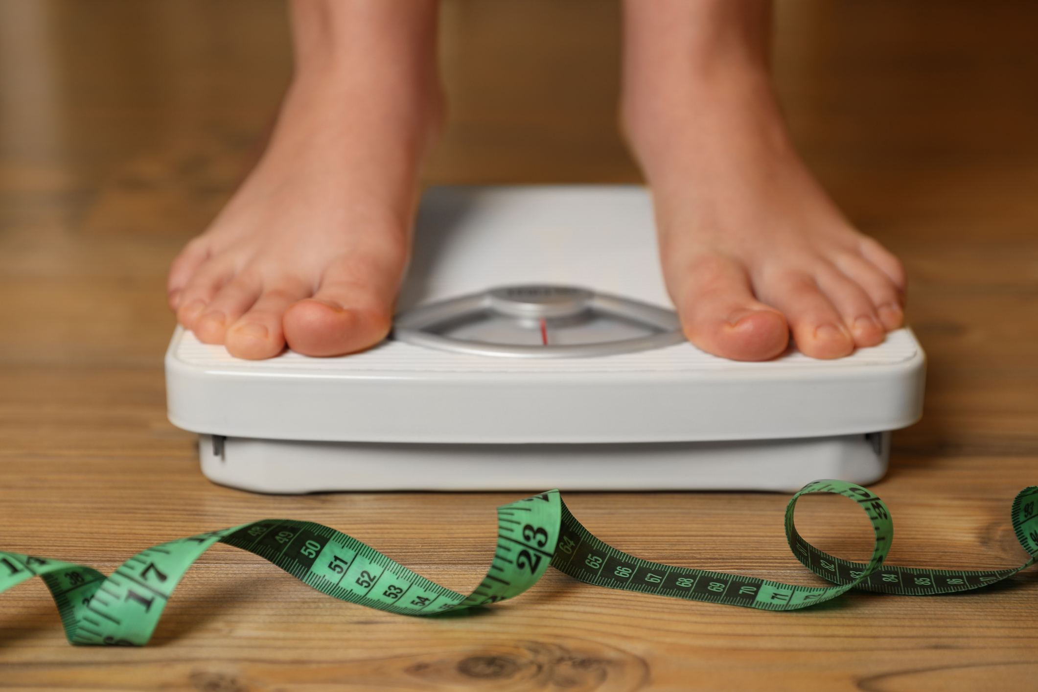Person using scale near measuring tape on wooden floor, closeup.