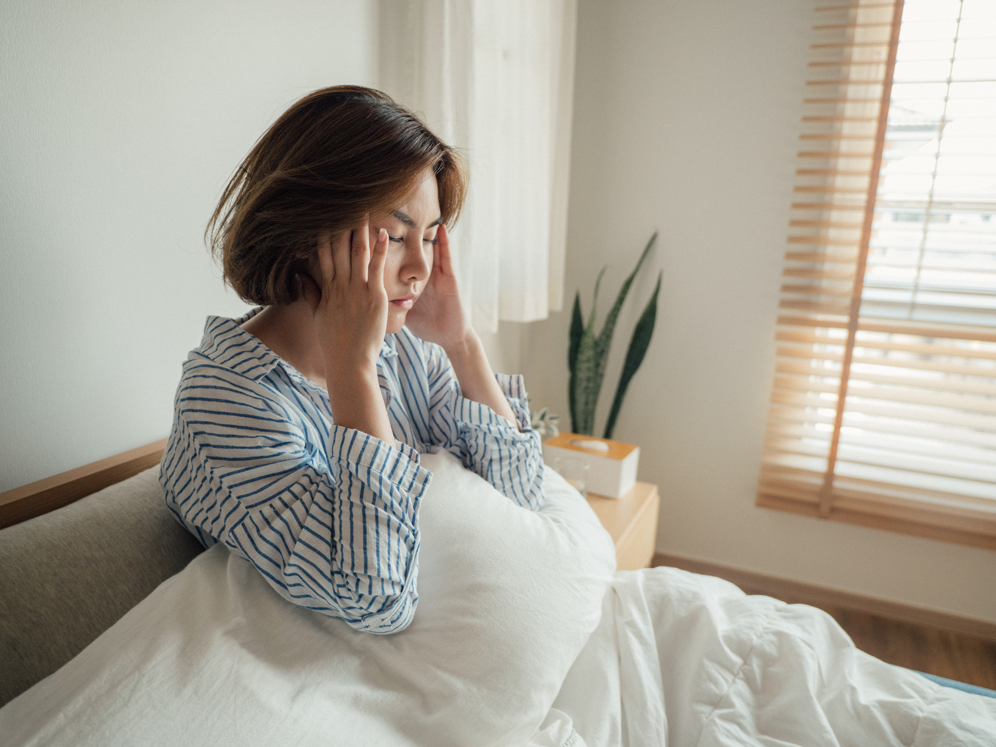 Young woman sitting up and holding head in bed.
