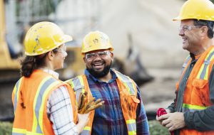 A group of three workers at a construction site wearing hard hats, safety glasses and reflective clothing.