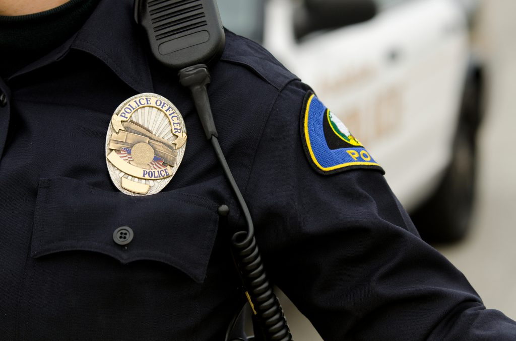 a close up of an officers uniform and badge with a patrol car in the background.