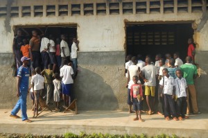 Children and other villagers look into a school showing monkeypox video