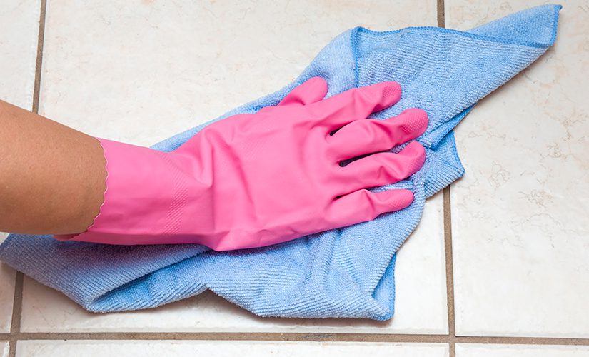 Hand in pink protective glove wiping tiles with rag in the bathroom.