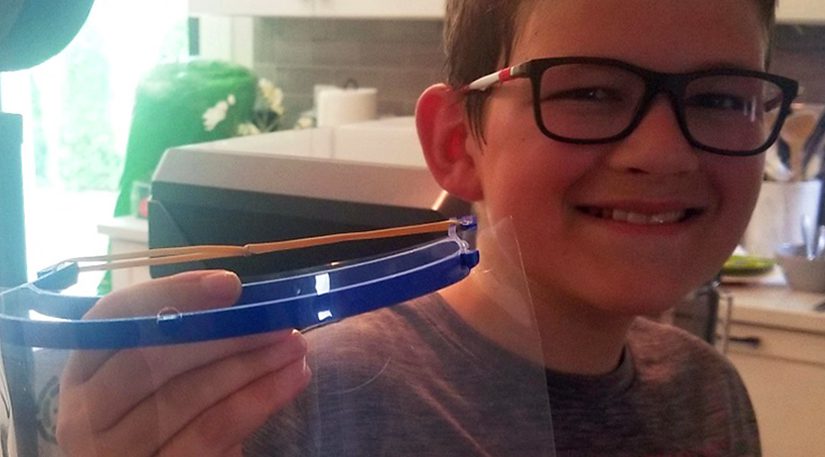 Boy holds up a face shield he made on a 3D printer