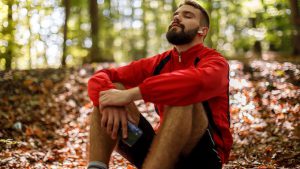 A man sits in the woods with his eyes closed.