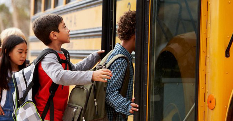 Kids stand in line waiting to board a school bus.