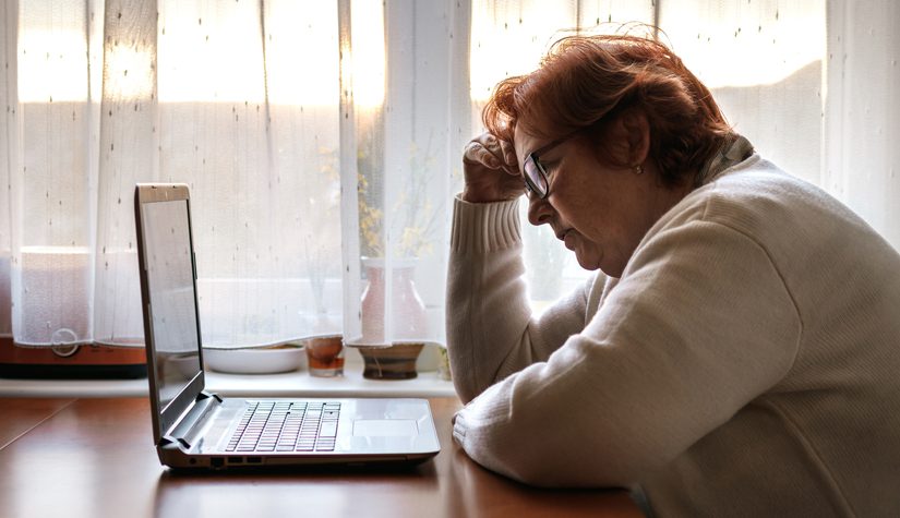 A worried looking older woman stares at a laptop computer.