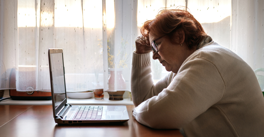 A worried looking older woman stares at a laptop computer.