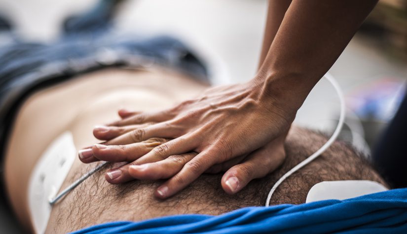 A close-up of hands performs cardiopulmonary resuscitation on a person lying on the ground.
