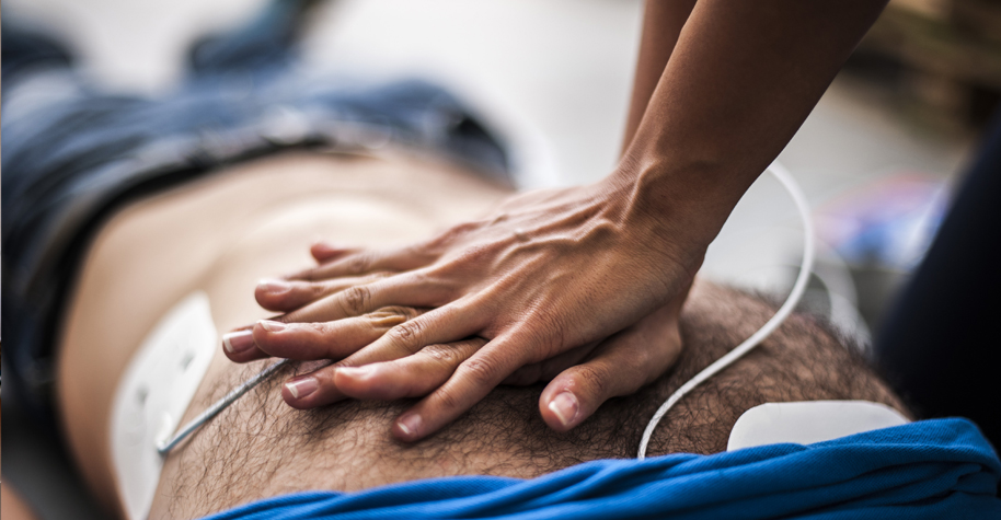 A close-up of hands performs cardiopulmonary resuscitation on a person lying on the ground.
