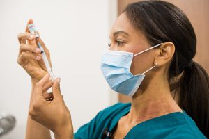 Female healthcare worker wearing a facemask and using needle and syringe to draw up dose from a vaccine vial