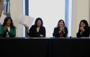 Four people sit at a conference table. One holds up a copy of the new Argentina law to combat AR while the others applaud.