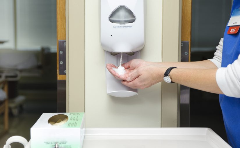 healthcare worker in a medical facility using touchless hand sanitizer