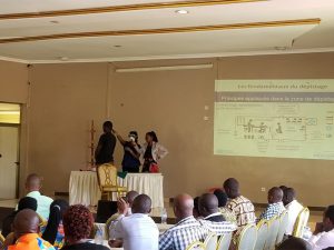 Healthcare workers wearing protective gear learn how to screen a possible Ebola virus patient in Kigali. The title of the slide translates to “fundamentals of screening”