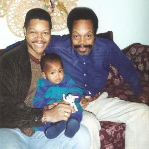 Photo of Demetrius Parker in 1996 holding his young son Vitthal, and seated next to his late father John H. Parker, Sr.