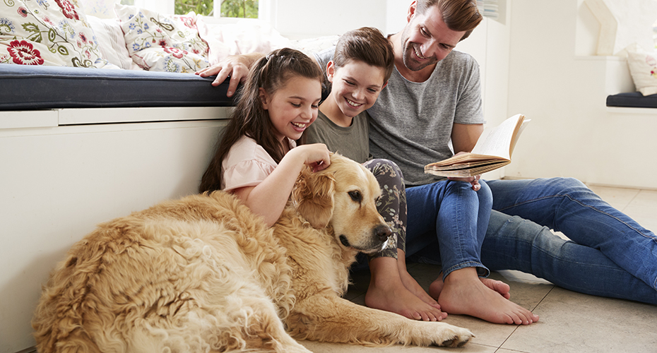 Father Reading Book With Son And Daughter And Pet Dog At Home