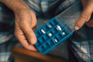 The hands of an elderly man holding a pill organizer