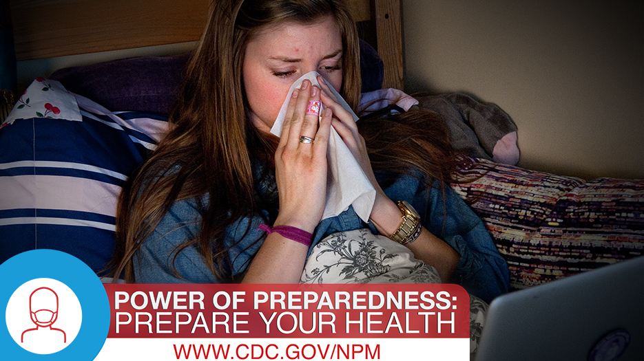 Young woman under the covers in bed blowing her nose.