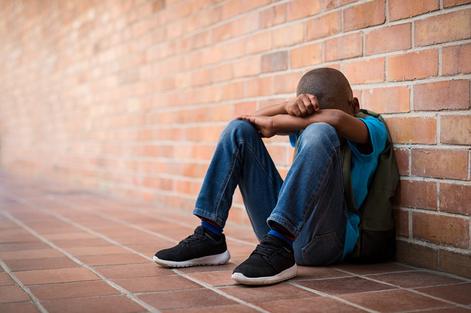 Sad boy sitting against a brick wall with his face hidden