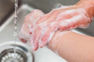 Unseen woman washing her hands with soap in a sink.