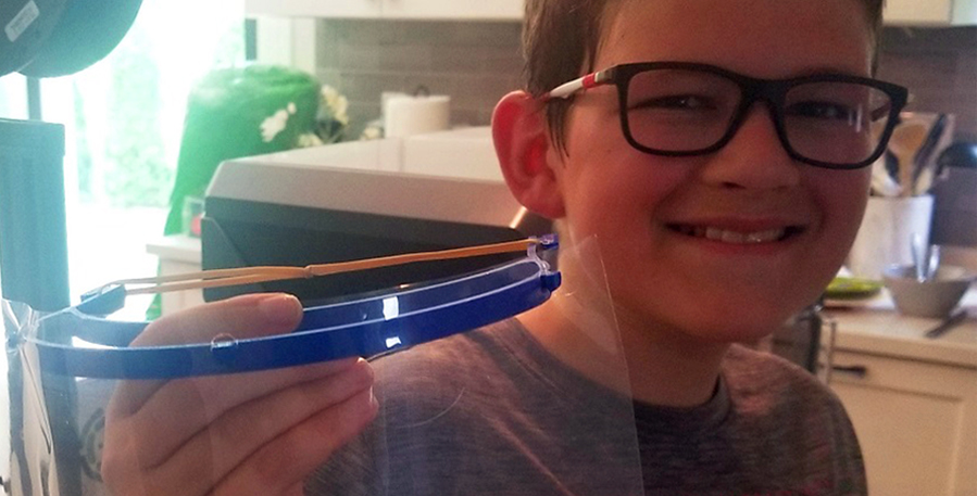 Boy holds up a face shield he made on a 3D printer