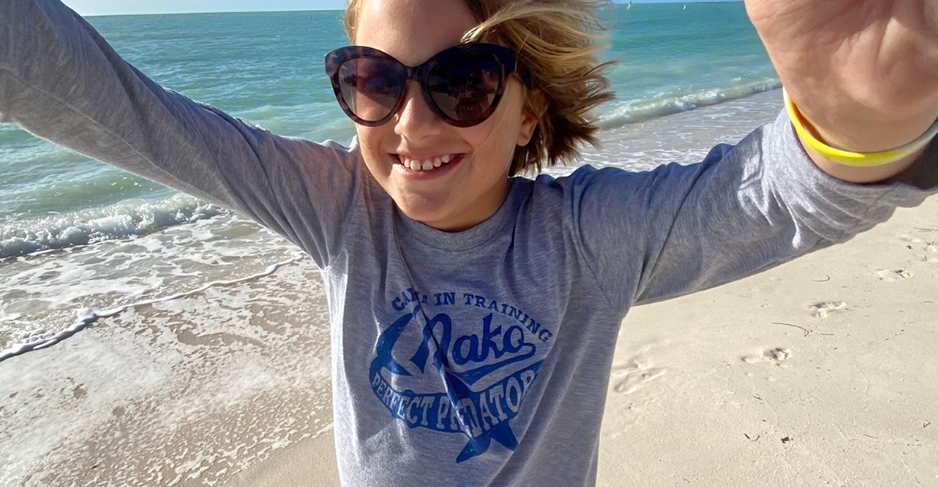 A young girl wearing sunglasses on the beach.